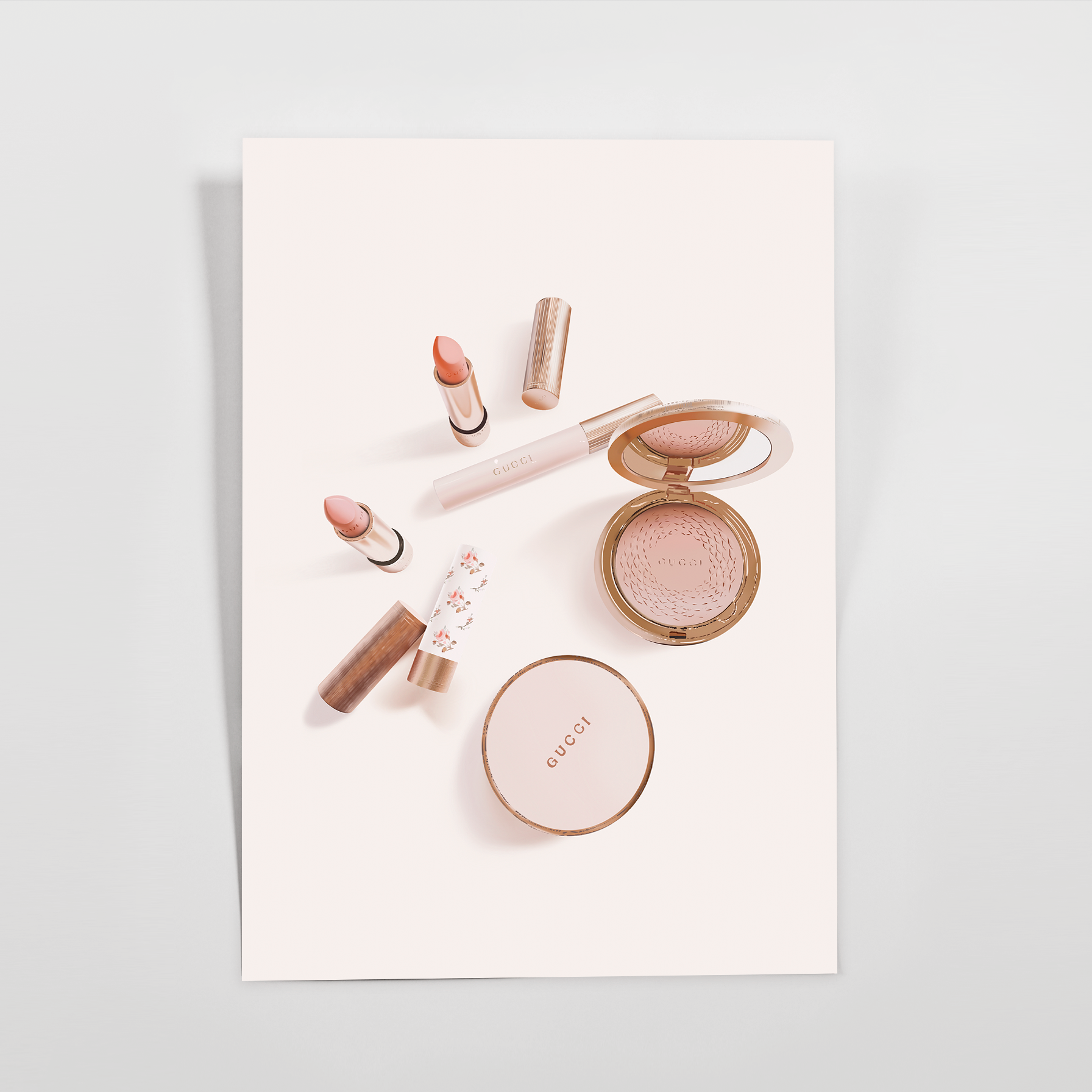 Blush journaling card with rose gold lipsticks, a lip gloss, an open powder compact with mirror, and a round cushion case